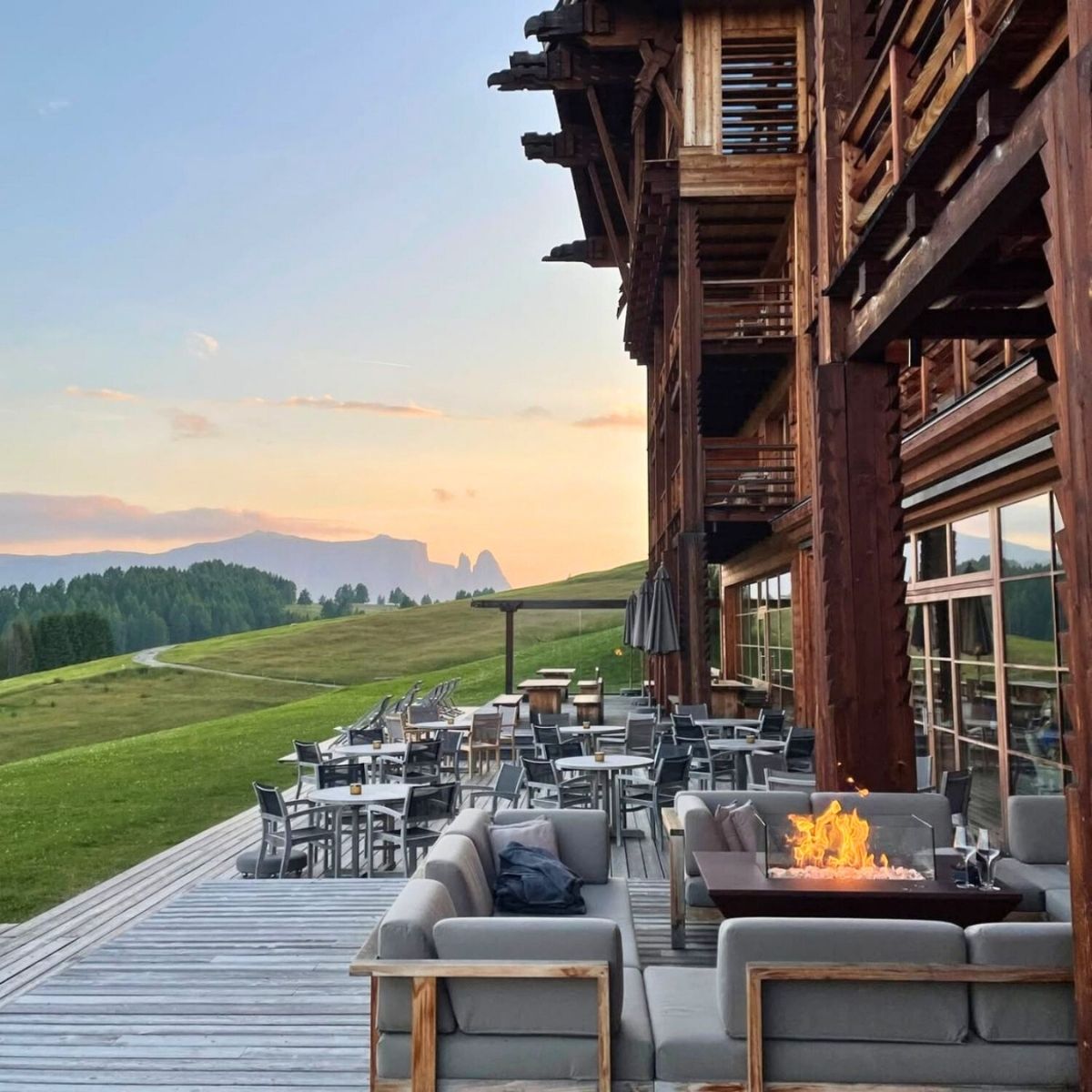 lodge with a wooden deck surrounding by mountains and the sunset