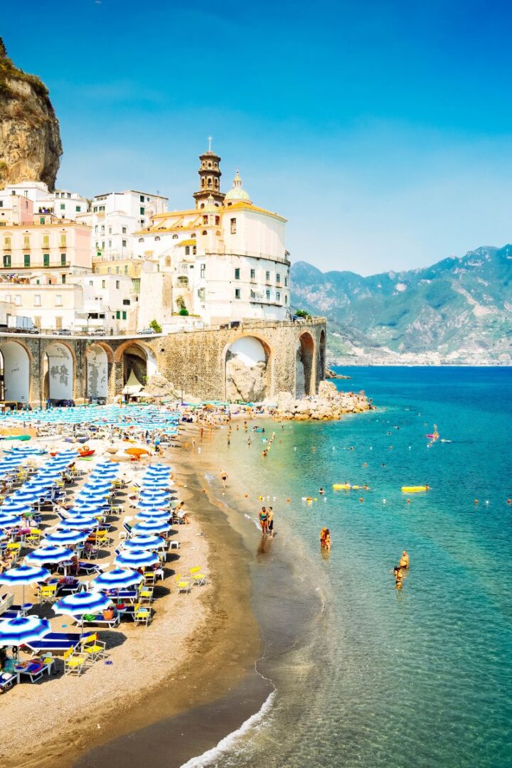 sandy beach with blue and white beach umbrellas with a white cliffside town in the background