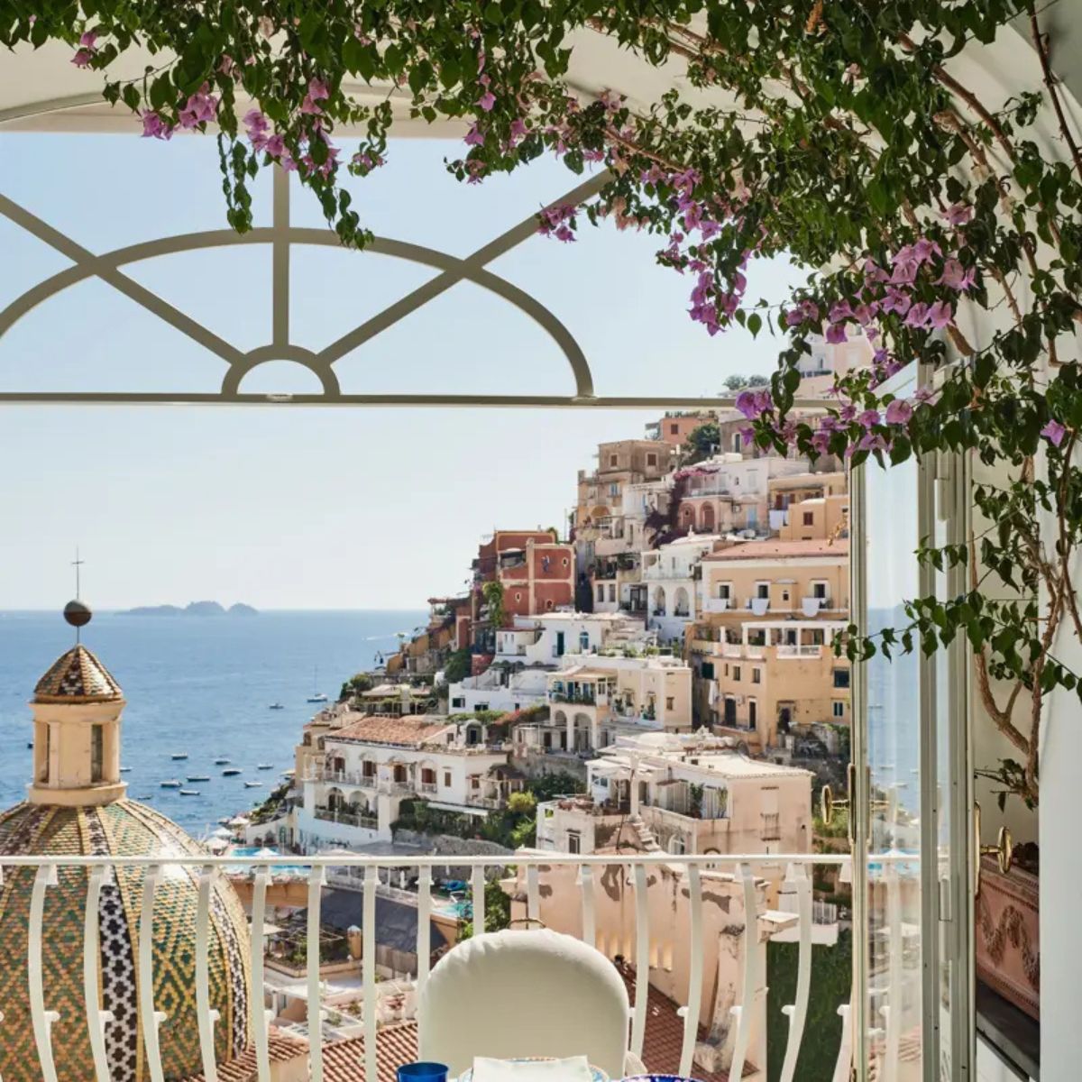 table and white iron gate with the town of positano in the background