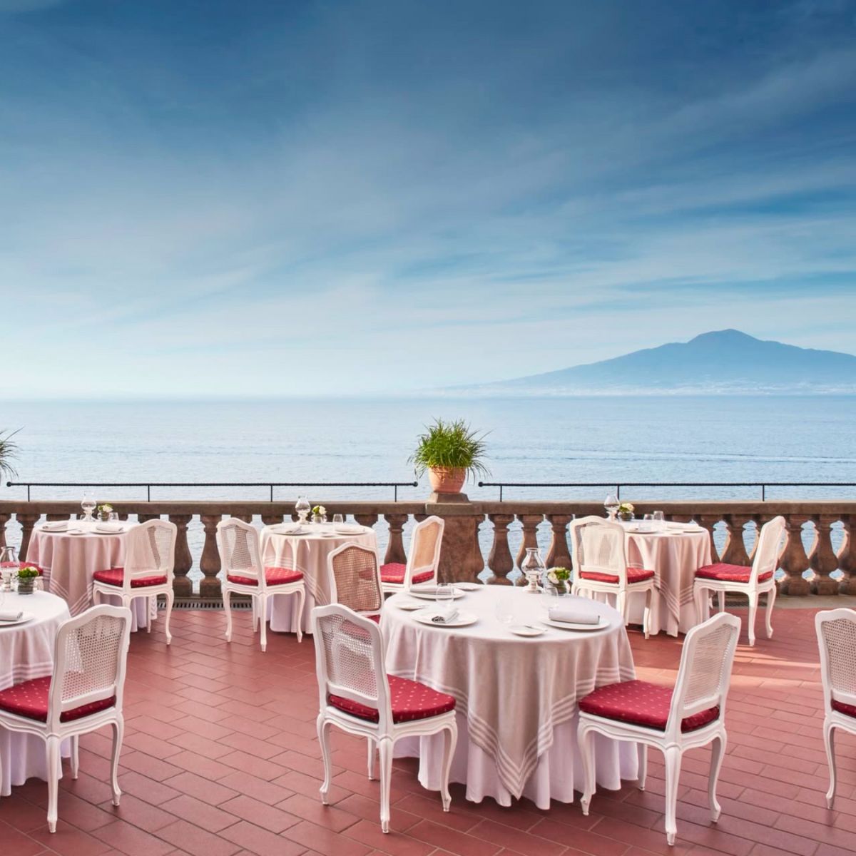 white table cloth tables with red chairs on a patio overlooking the sea