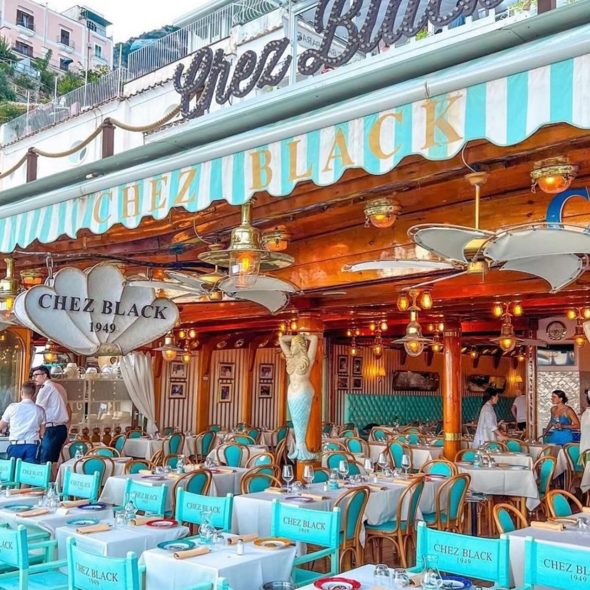 light blue and white tables and chairs with a striped awning and a Chez Black sign