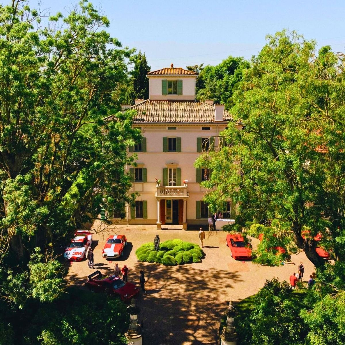 stone building flanked by green trees with vintage cars in front