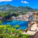 island of ischia with green mountains and blue water and a pastel town