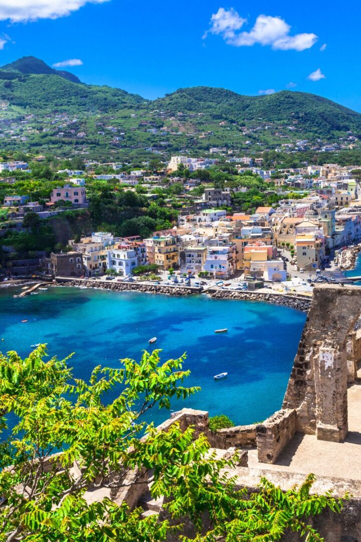 island of ischia with green mountains and blue water and a pastel town