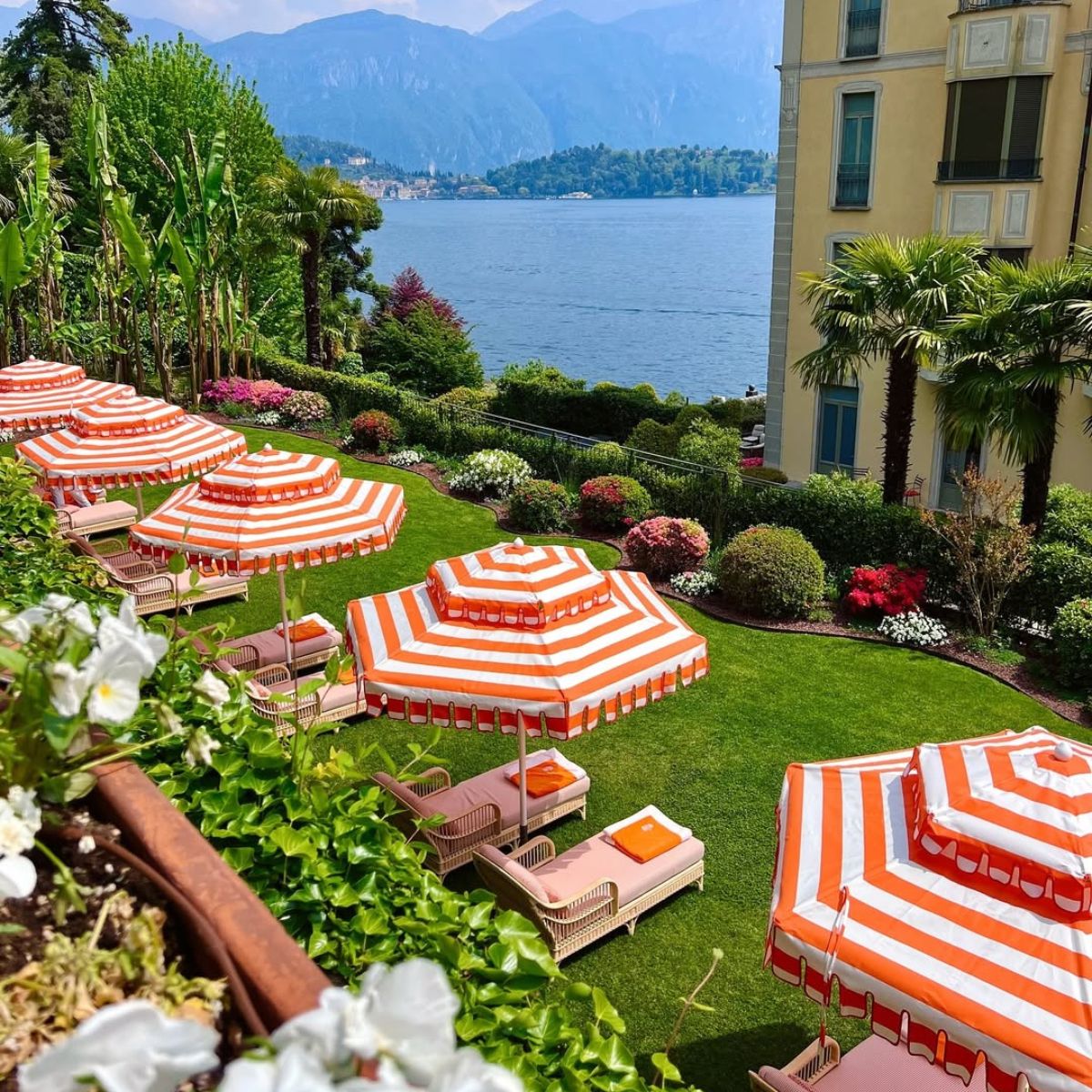 orange and white umbrellas and lounge chairs on green grass with the lake in the background