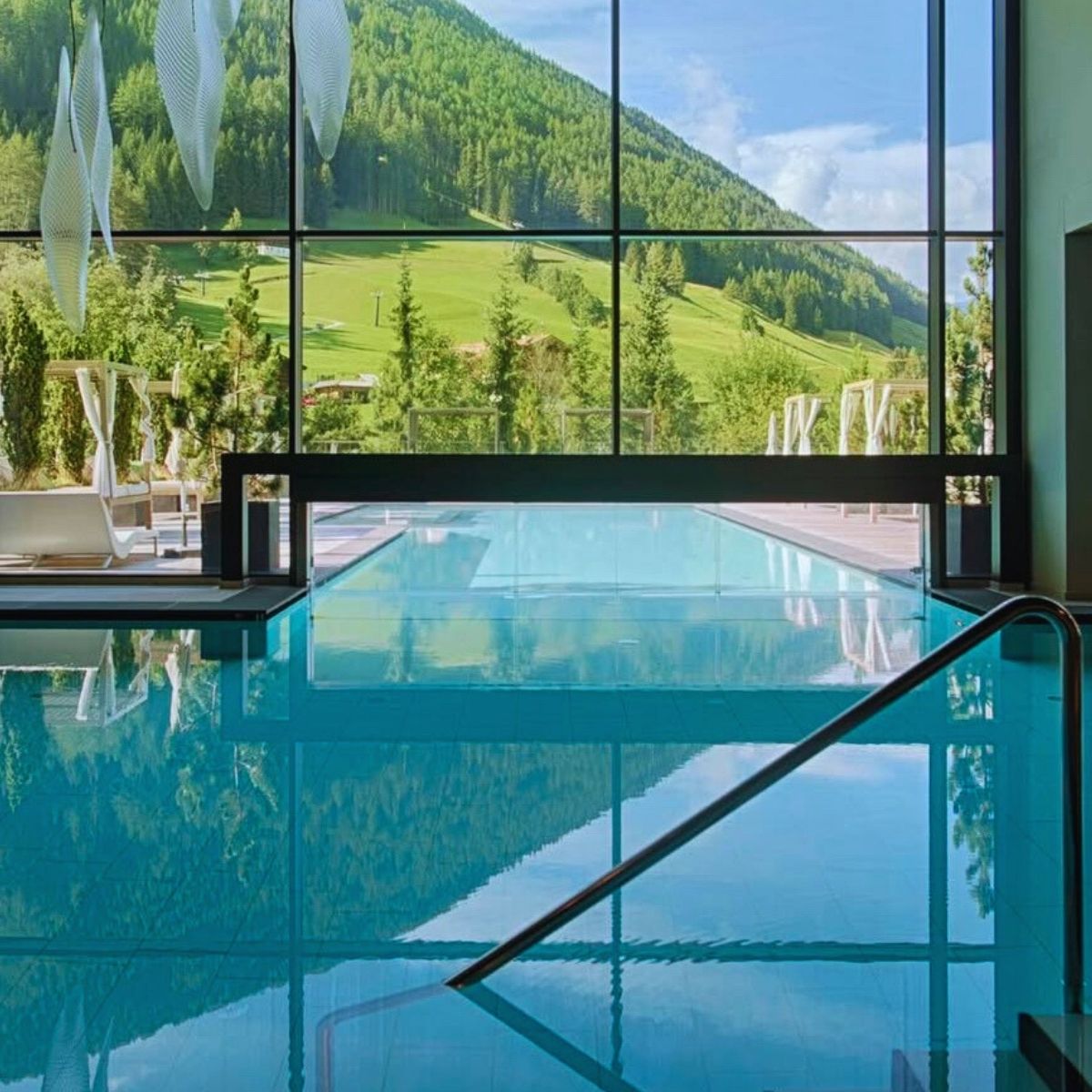 indoor swimming pool with large windows showing the green mountains