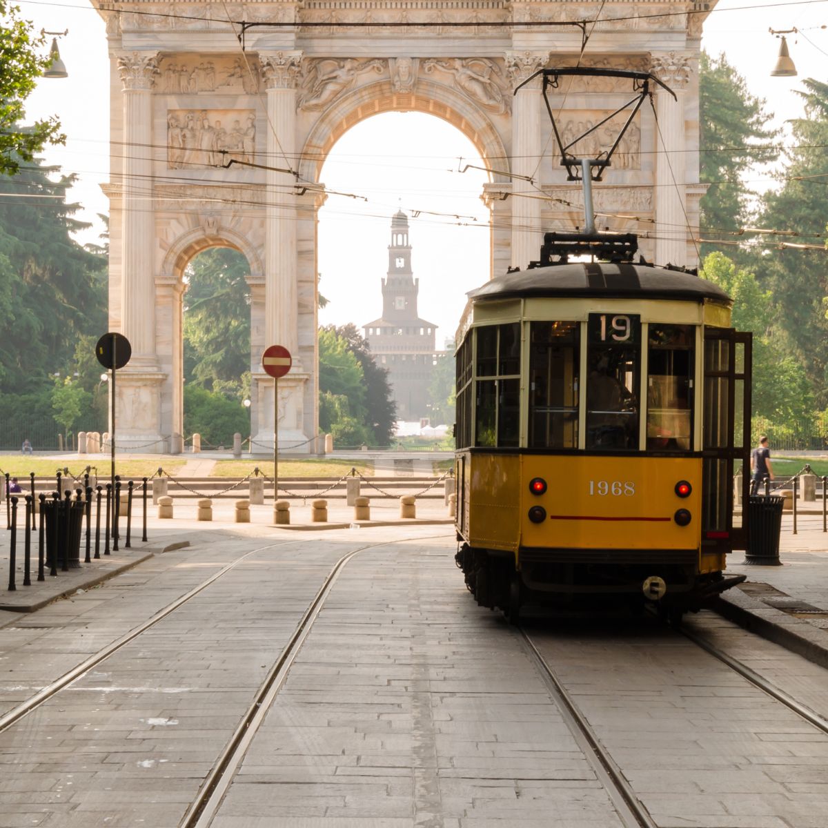 yellow street car with stone arch in the background