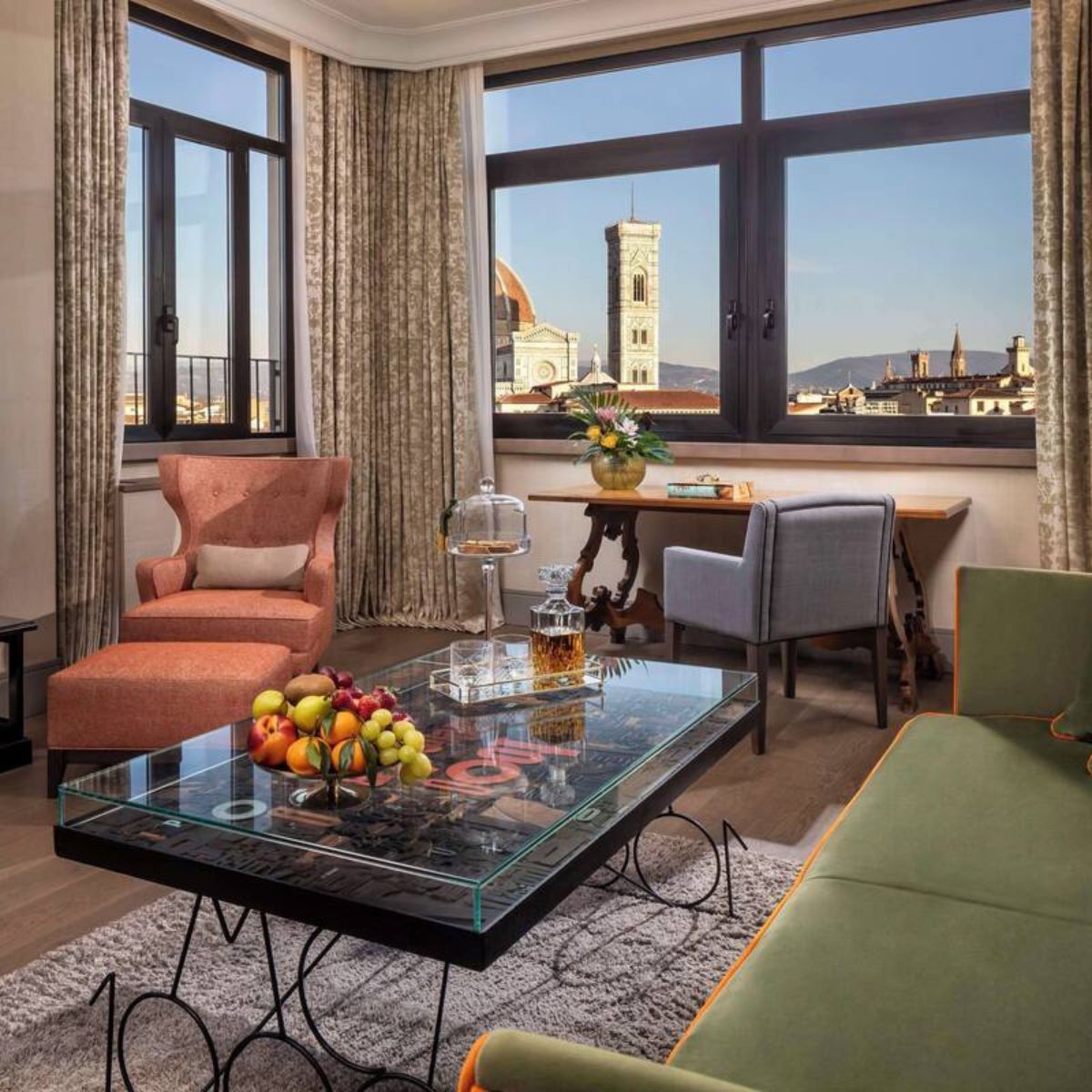 hotel room with a green couch and coral arm chair with windows overlooking Florence