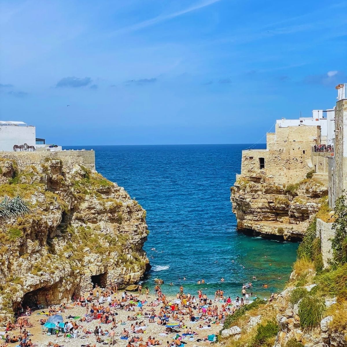 crowded sand beach in between stone cliffs