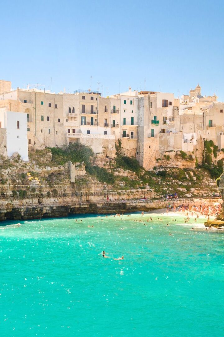 green sea and beach with cliffs and building in the background