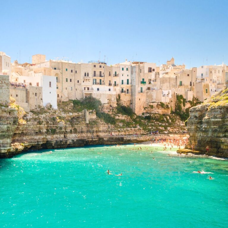 green sea and beach with cliffs and building in the background
