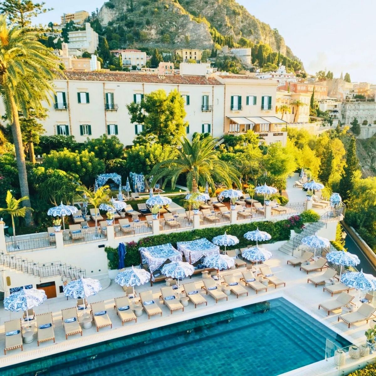 swimming pool with blue and white umbrellas in sicily cliff