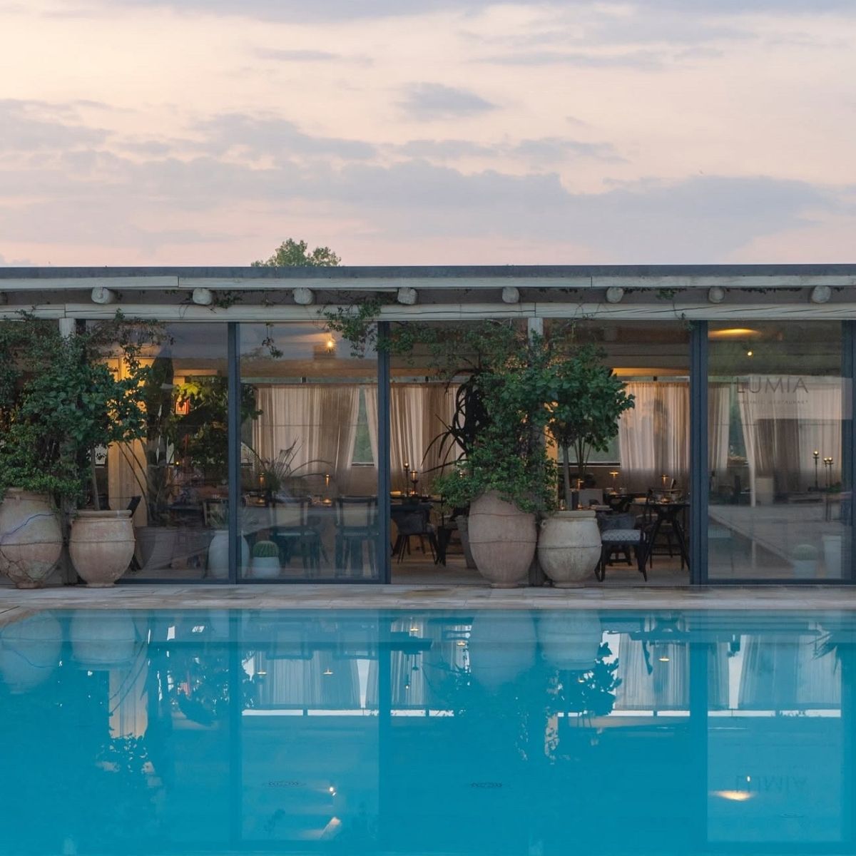 pool with a restaurant with glass windows and large potted plants in the background