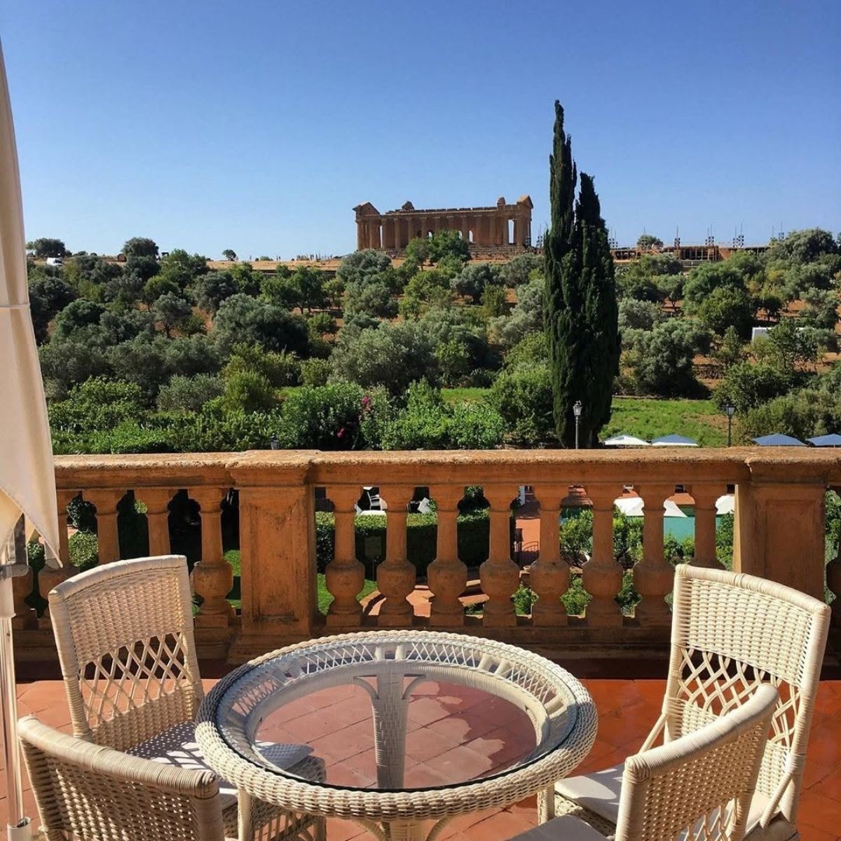 table and chairs on a patio with the valley of temples greek columns in the background