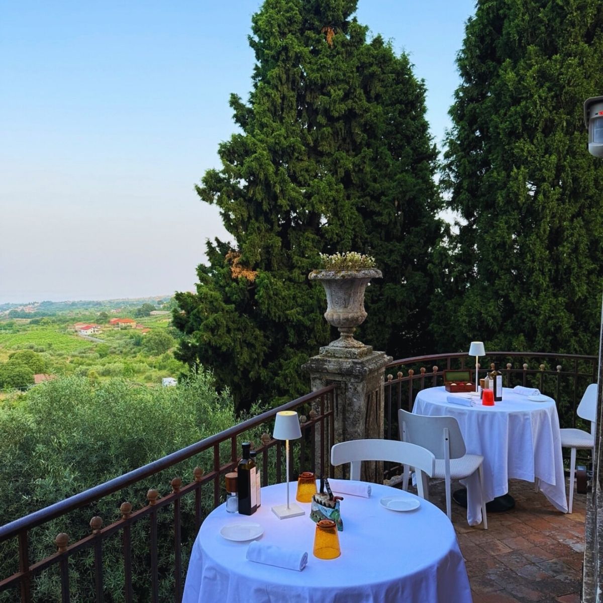 two circle dining tables with white table cloths on an outside terrace overlooking a vineyard