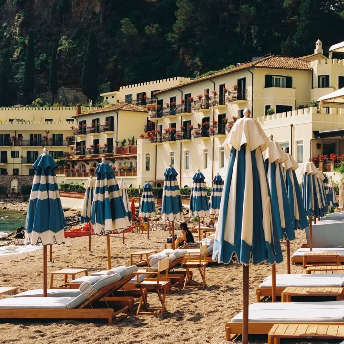 sandy beach with lounge chairs and blue and white umbrellas