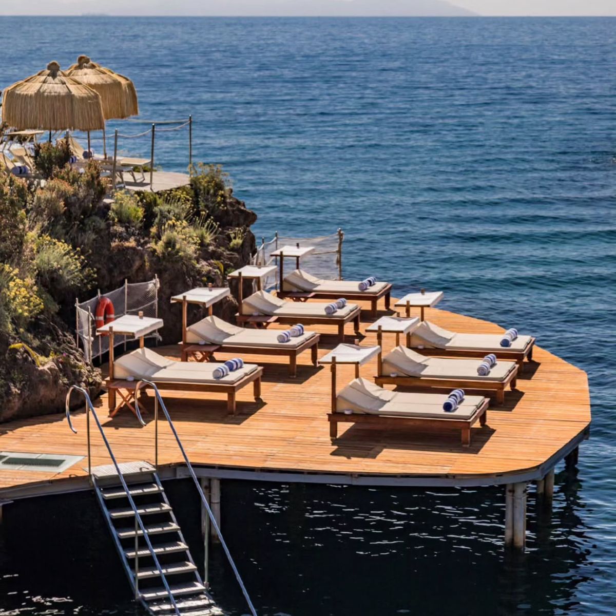 Beach club sun loungers on a wooden deck over crystal clear Ischia waters