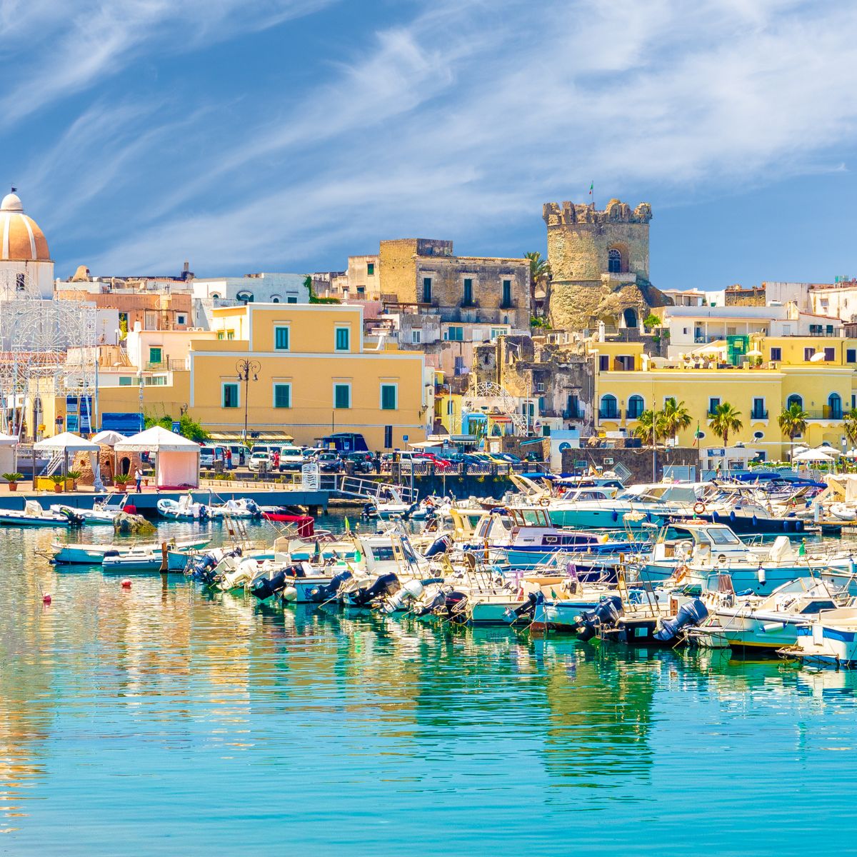 Pastel-colored town of Ischia with boats in the harbor and green mountains behind